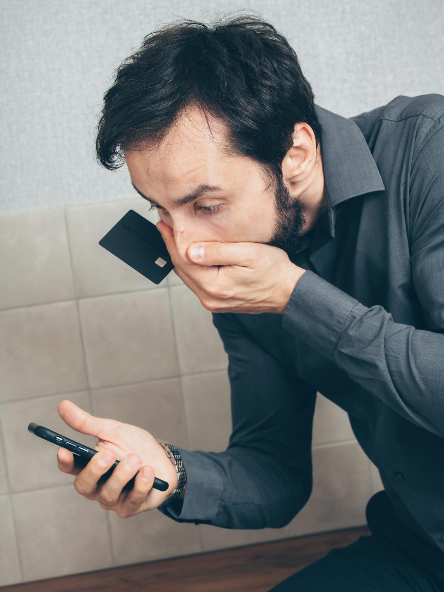 Man in shock discovering possible fraud or data breach with smartphone and credit card.